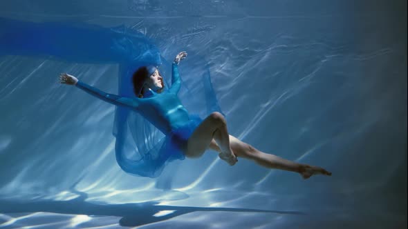 Attractive Young Woman Swims Beautifully Underwater in a Blue Dress Dress