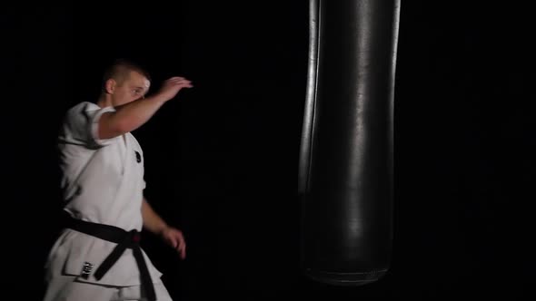 Black Belt Karate Man Practicing on the Sandbag on Black Background