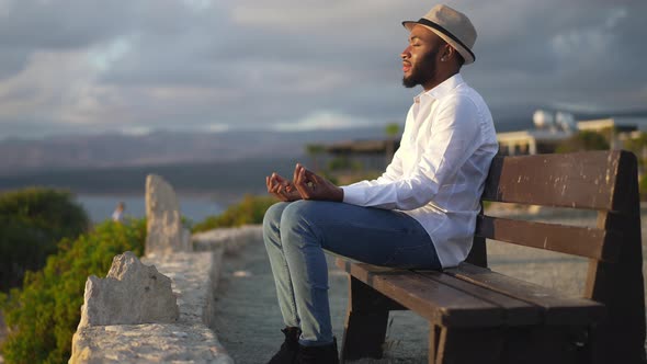 Side View of Calm Confident African American Gay Man Meditating with Closed Eyes Sitting at Sunset