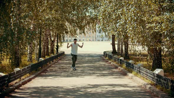 Young Attractive Man with Tattoos Dancing in the Park on the Path - Buildings on the Background