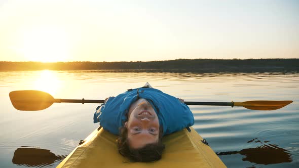 Happy Young Man Is Resting Lying on Kayak, Relaxing in Calm Lake with a Paddle 