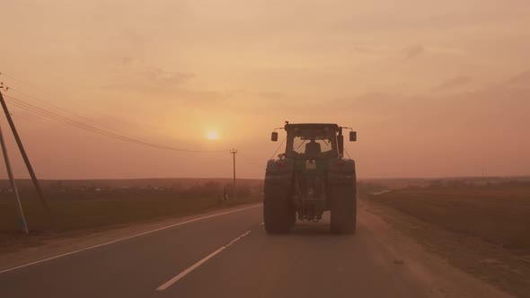 Farm tractor with large wheels driving on country road at sunset after sowing or harvesting 