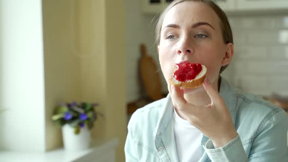 Beautiful Woman Eating a Delicious Jam Sandwich at Home in the Kitchen