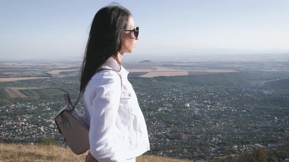 Young Woman with Backpack Standing on Cliff and Looking To a Sky