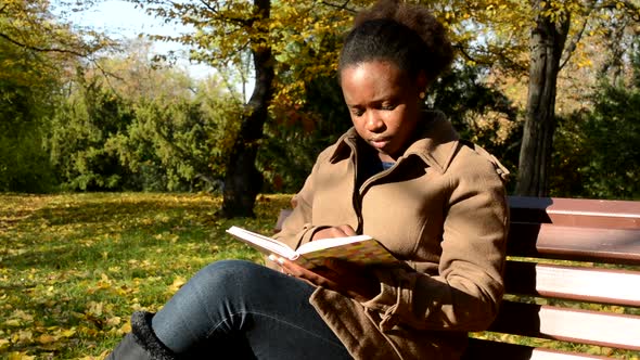 Young Beautiful African Calm Girl Sits on Bench in Woods, Examines Book and Observes Landscape