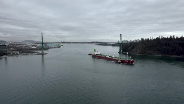 Red barge passing under Lions Gate bridge with Vancouver city in background, Canada. Aerial drone vi