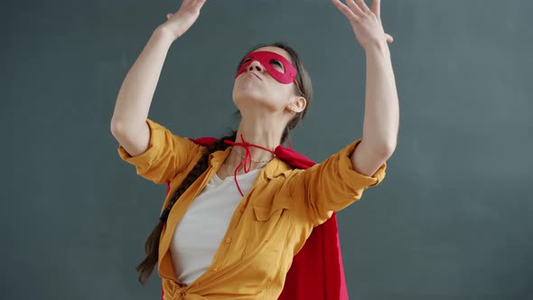 Slow Motion of Young Woman Wearing Superhero Costume Red Cape and Mask Moving on Gray Background