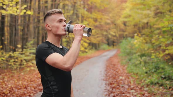 The Athlete is Standing on a Forest Road and Drinking Water From a Bottle