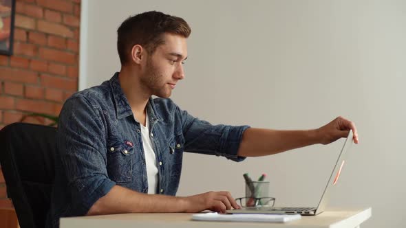 Side View of Handsome Young Man Sitting at Desk Opening Laptop and Starts Typing on Keyboard of