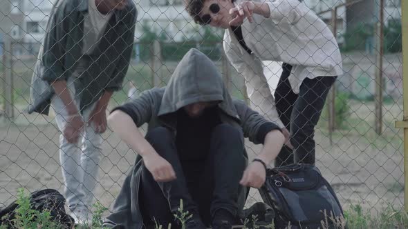 Caucasian and African American 1990S-styled Men Bullying Young Curly-haired Guy Sitting at Mesh