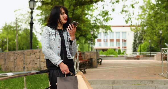 Brunette woman holding paper shopping bags and talking by phone