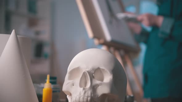 A Young Woman Artist Drawing a Painting in the Art Studio - a Skull and Other Figures on the Table