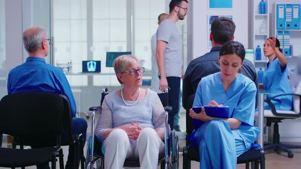 Nurse Filling Documents While Talking with Disabled Senior Woman