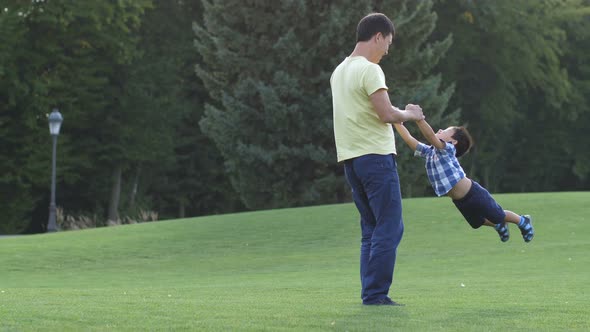Happy Asian Father Spinning His Cute Son on Meadow