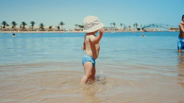 Sweet Baby Boy Making First Steps in Seawater. Cute Toddler Splashing Water