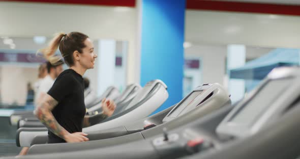 Young Woman Running on a Treadmill at Gym. Side View. Woman Training at Fitness Center. Woman