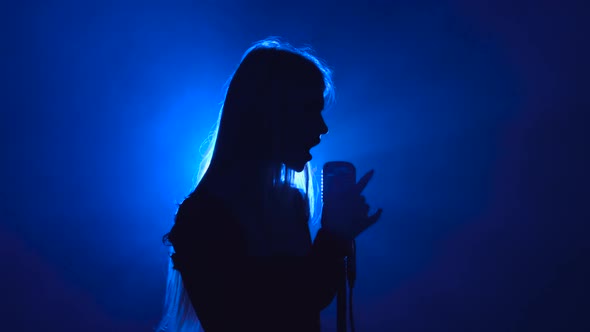 Girl in Singing in Retro Microphone Hilarious Song. Smoke Background. Silhouette. Side View