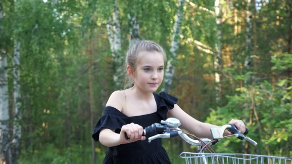 Teenage Girl in Dress Learns to Ride Bike in Park at Sunset