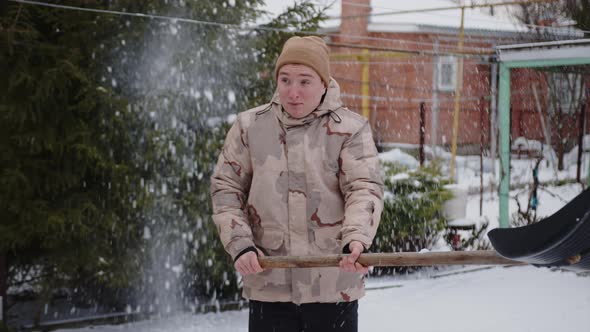 Cheerful Young Guy Throws Snow with a Shovel