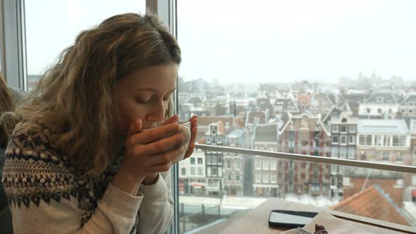 Young Woman Sips Coffee and Looks at Amsterdam Panorama