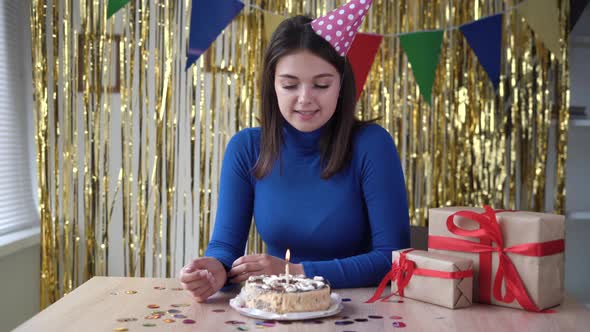 Young Woman Celebrating One Birthday Rejoices and Blows Out the Candle on the Anniversary Cake