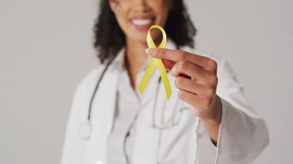 Video of smiling biracial female doctor holding yellow bladder cancer ribbon