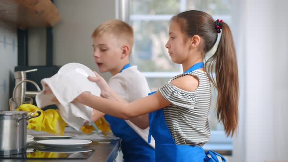 Brother and Sister Kids in Apron Washing Dishes in Modern Home Kitchen