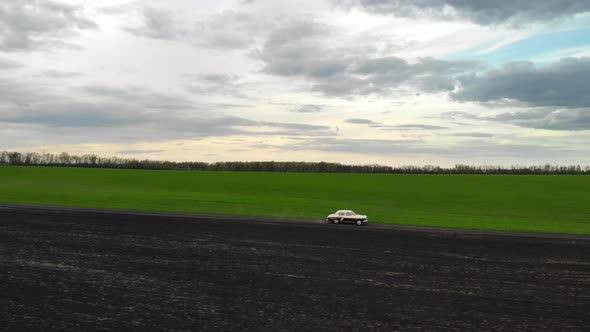 Beautiful Retro Sedan of Beige and Burgundy Rides on Road in Green Field