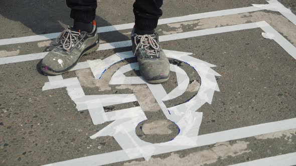 Male Worker Stepping on Disabled Car Parking Lot Sign Outlined with White Tape