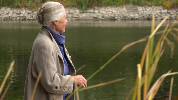 An Elderly Woman Plays Stone Skipping at a Lake and Laughs