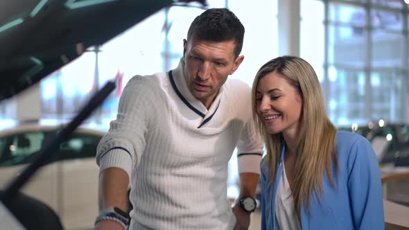 Positive Woman Talking with Concentrated Man Examining Open Car Trunk in Car Dealership