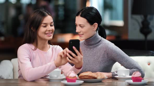 Female Friends Gossiping Scrolling Social Networks Smile at Cafeteria