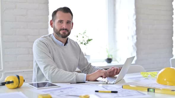 Young Architect with Laptop Smiling at Camera in Office