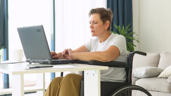 Motivated Senior Freelancer is Working Typing in Laptop Sitting in Wheelchair at Home