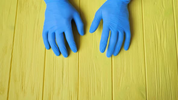 Blue Gloved Hands Closeup on Yellow Wooden Table