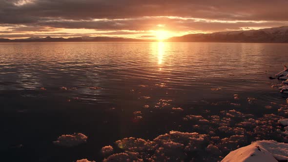 Ice floating on shoreline during golden sunset over lake