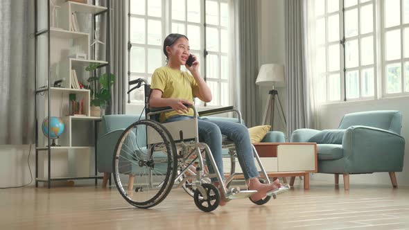 Asian Kid Girl Sitting In A Wheelchair And Talking On Phone At Home