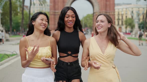 Three Beautiful Joyful Women Best Friends Walking Arm in Arm on City Square and Laughing
