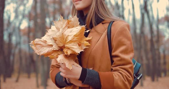 Girl Holds a Bouquet of Autumnal Leaves in Her Hands