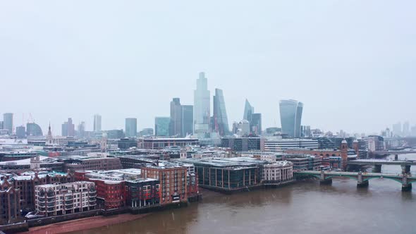 Rising London aerial drone shot of snow falling on city of London skyscrapers from river thames
