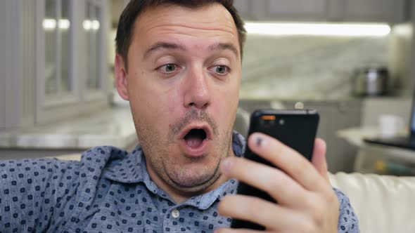 Joyful Excited Handsome Man Sitting on Couch Celebrating Online Lottery Win Alone at Living Room