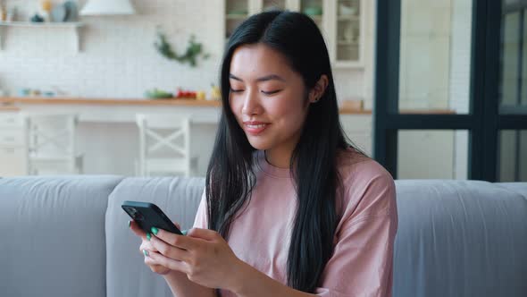 Young Thoughtful Dark Haired Asian Ethnicity Woman in Pink Tshirt Typing on Smartphone Sending Text