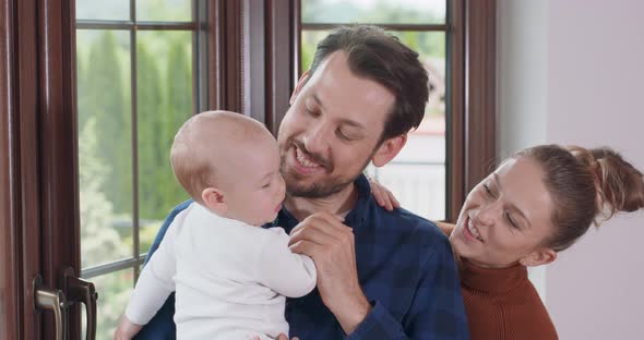 Young Happy Parents and Their Adorable Baby Next to the Window Bearded Father Holds His Baby and