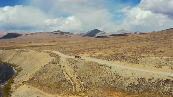 Aerial drone of a red suv driving along a dirt road path in the high-altitude alpine orange plain of