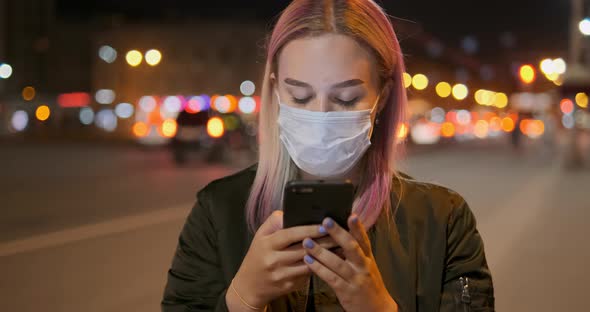 Woman Wearing Mask Looks in Smartphone Against Car Lights