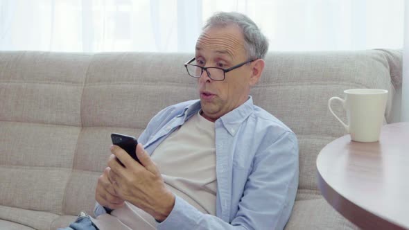 Elderly Man Rejoices Looking Into Smartphone