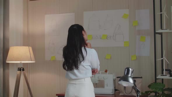 Asian Woman Designer Looking At The Design Sketch Paper On The Wall