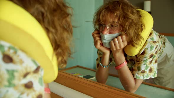 a Tourist is Looking at Herself in the Mirror in a Hotel Room and Fixing a Medical Protective Face