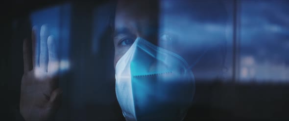 Man in a face mask looking out of a window during the isolation