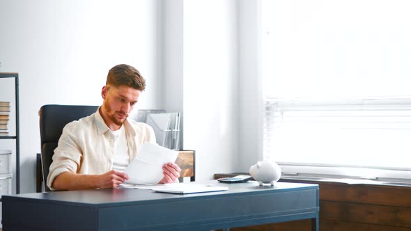 Bearded male financial director reads bank reports sitting at grey table